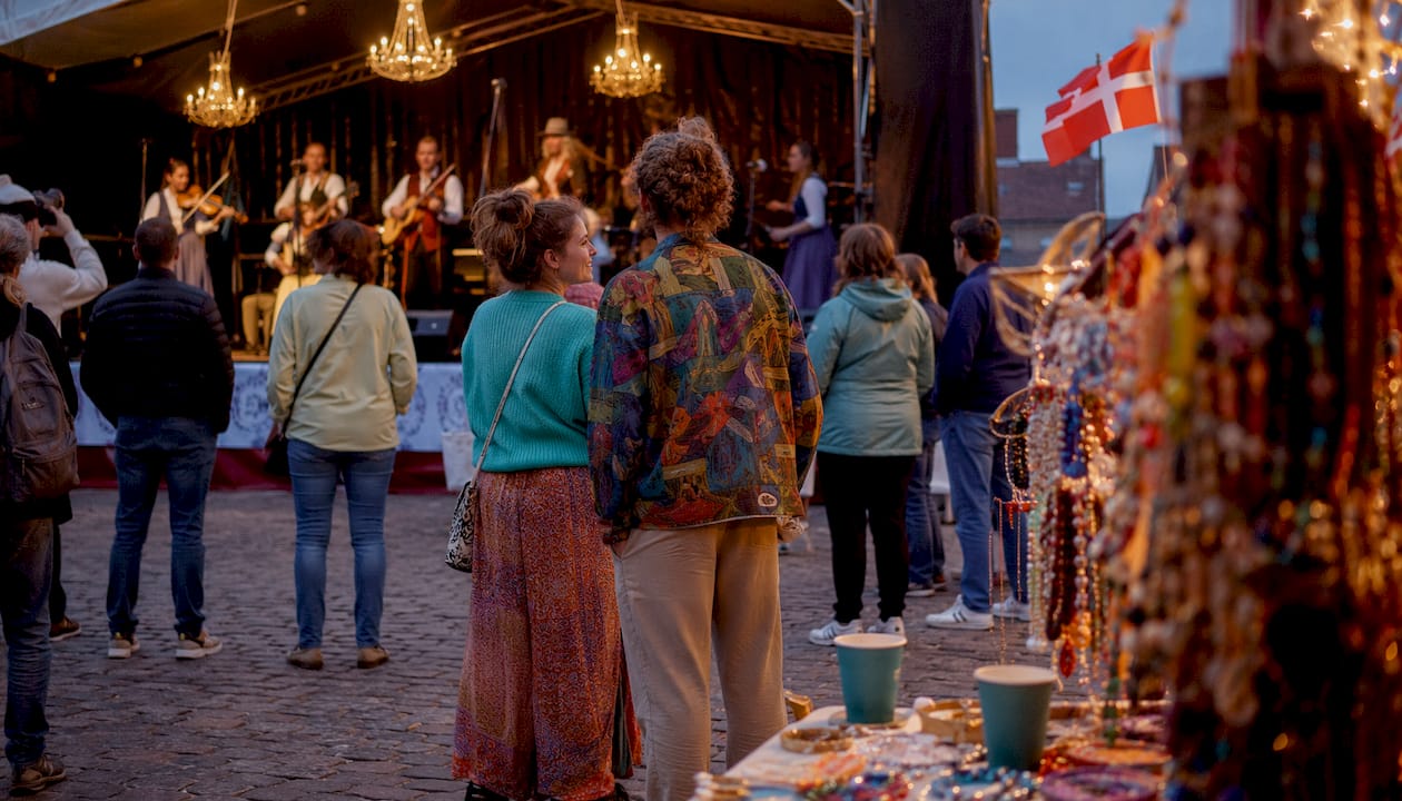 Glade mennesker samles under åben himmel til en lokal kulturfest, hvor danske traditioner og stemning er i centrum.