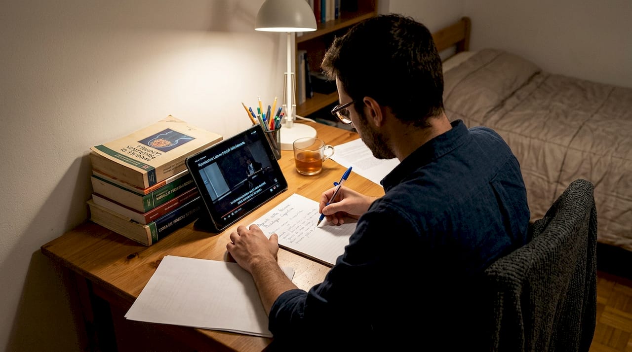 Un uomo si dedica allo studio delle lezioni online nella sua postazione di lavoro in camera da letto.