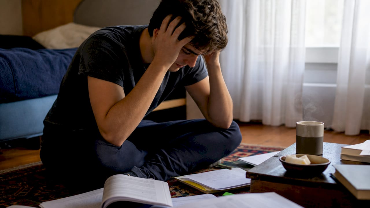 Studente sopraffatto dallo studio circondato da libri aperti in biblioteca