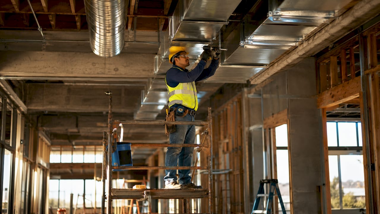 Construction worker installing HVAC ducts in ceiling