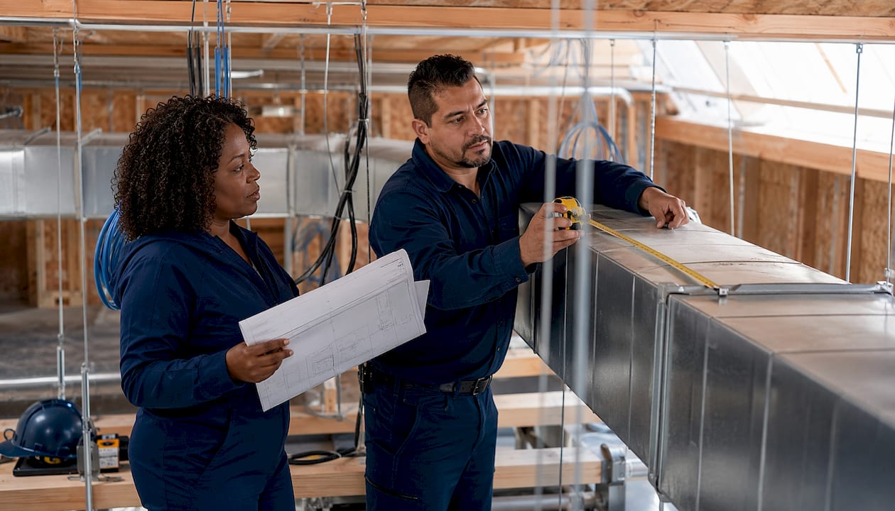 Engineers measuring HVAC ductwork in ceiling space