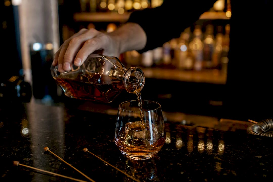 Whiskey being poured over ice in glass