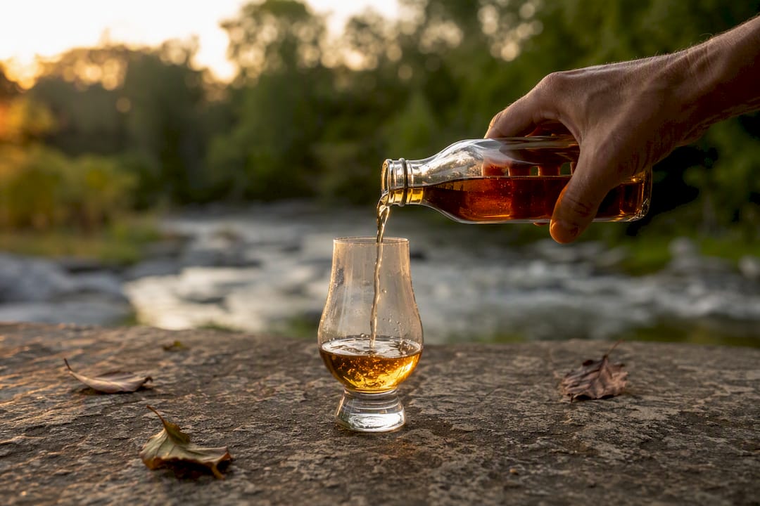 Hand pouring whiskey into tulip glass