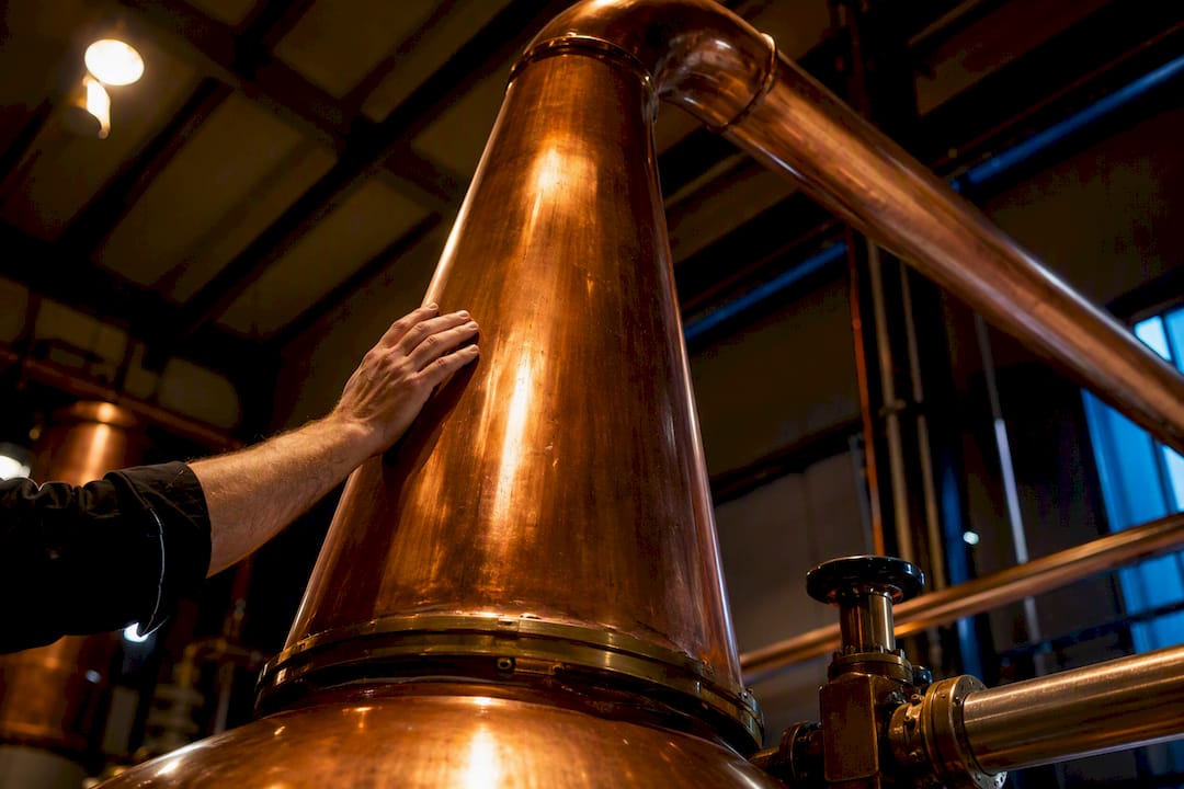 Hand inspecting a tall copper pot still