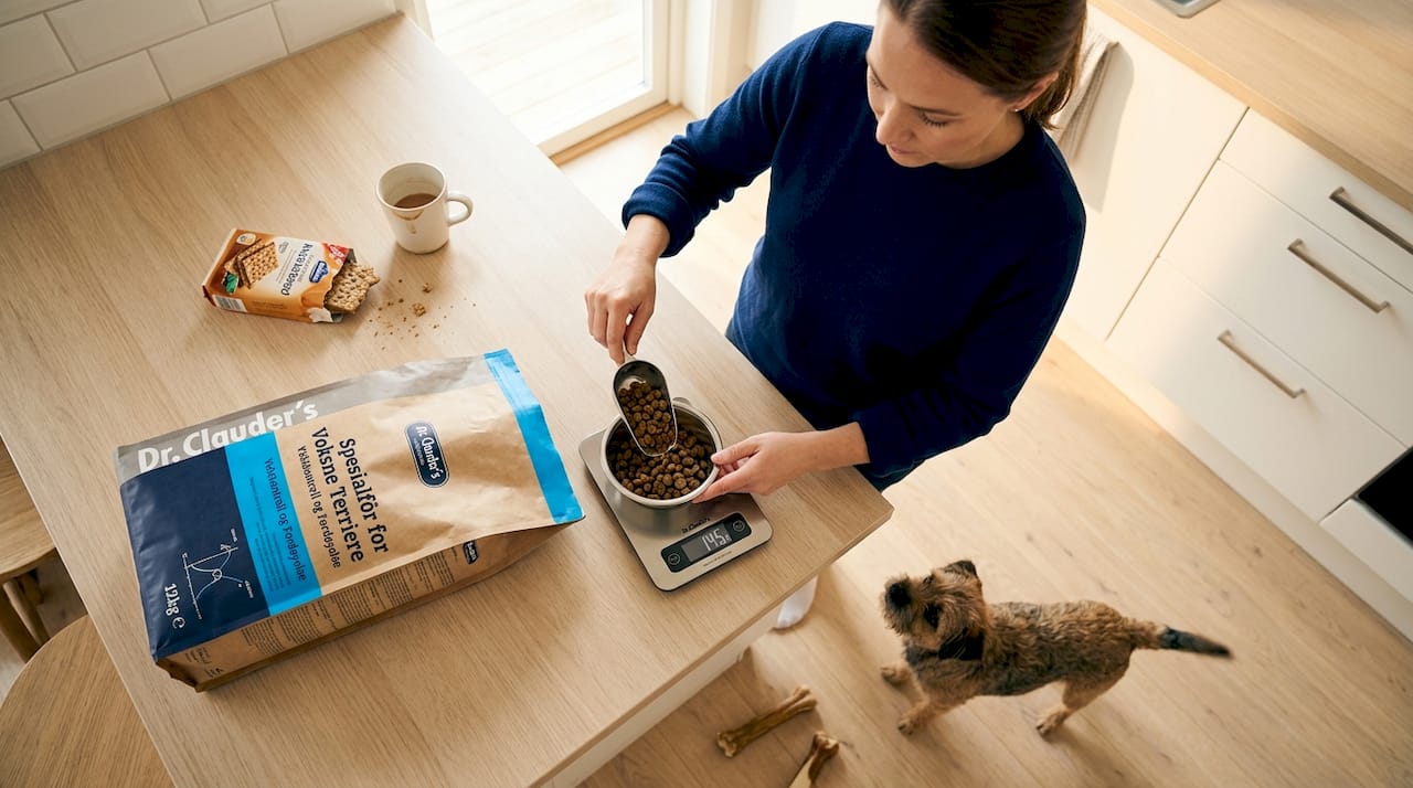 En hundeeier står på kjøkkenet og måler opp allergivennlig hundemat.