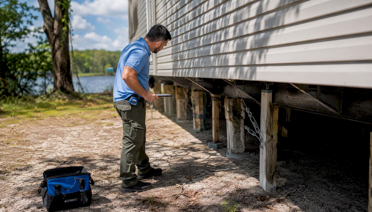Home inspector evaluating manufactured home foundation outdoors