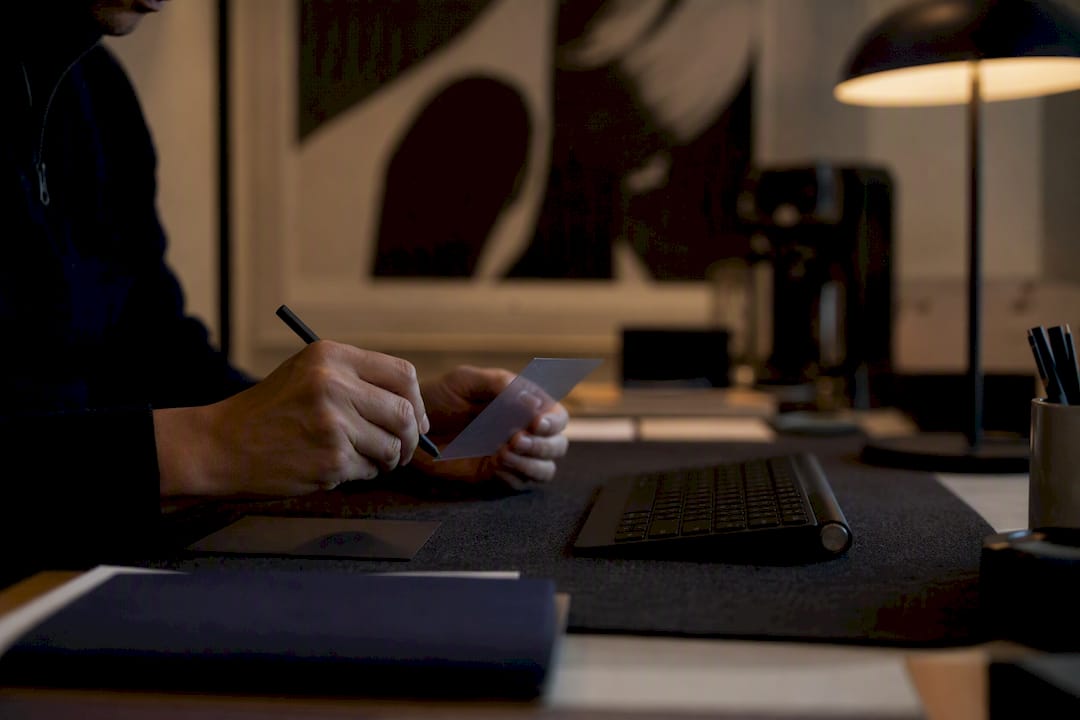 Hand holding pen over note card near keyboard