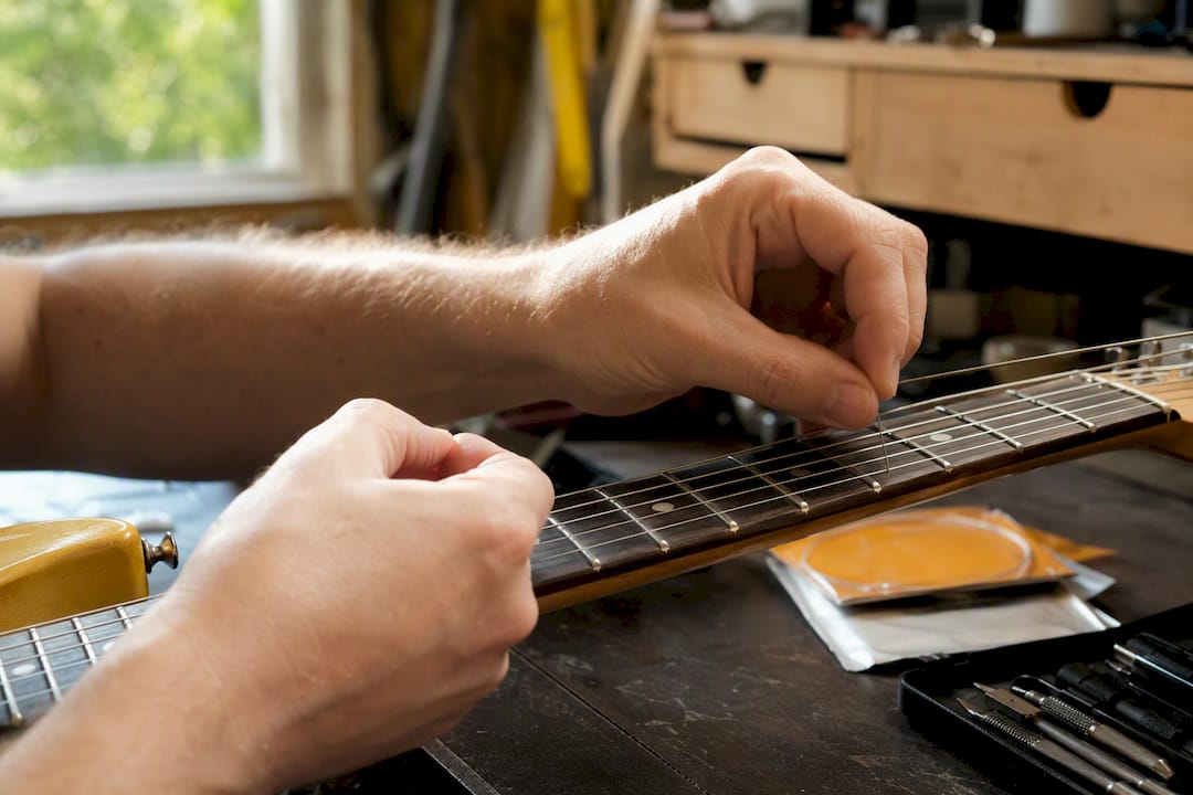 Hands stretching new guitar strings at 12th fret