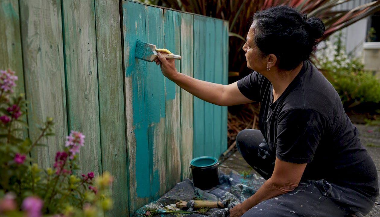 Hands painting wooden garden fence at home