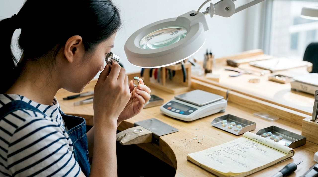 一位质检员正在工作台前仔细检查一枚欧泊戒指。