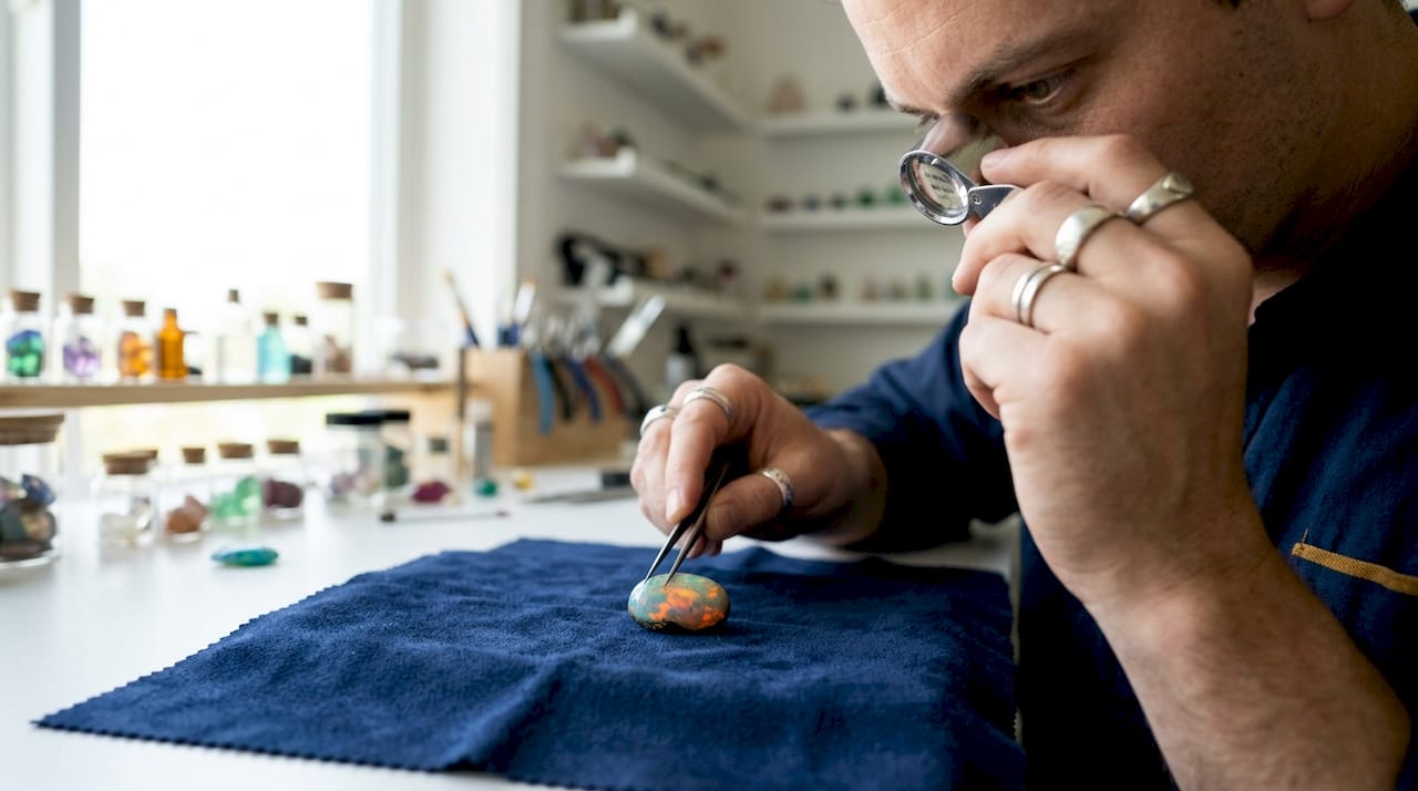 Close-up of hands inspecting opal with loupe