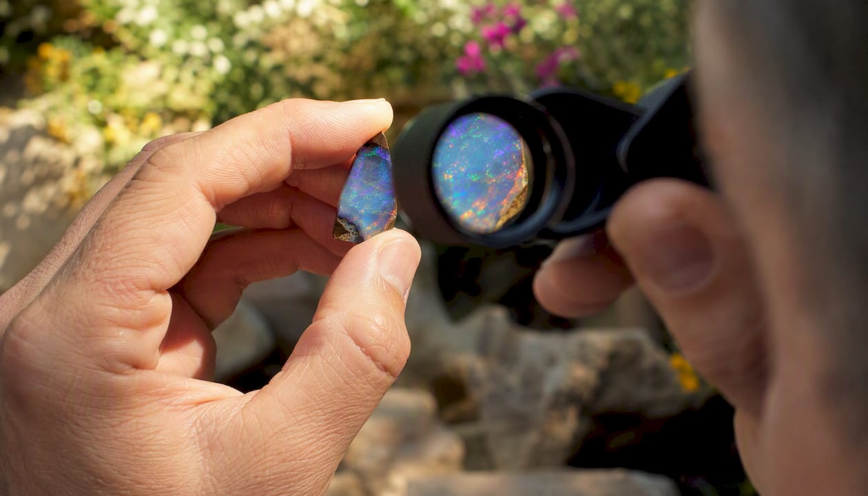 Hand holding black opal viewed through loupe