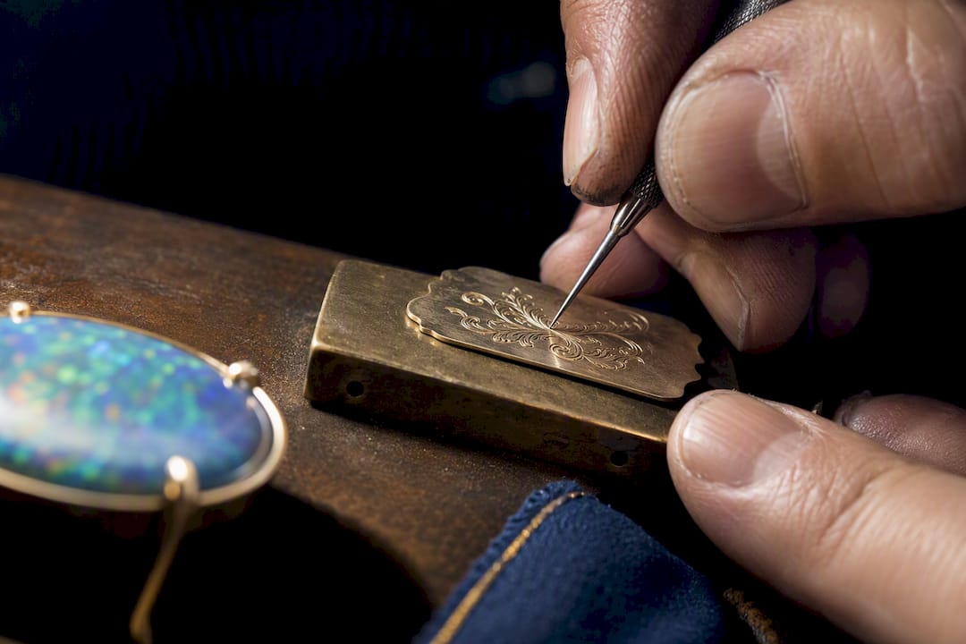 Jeweler engraving a metal plaque beside opal