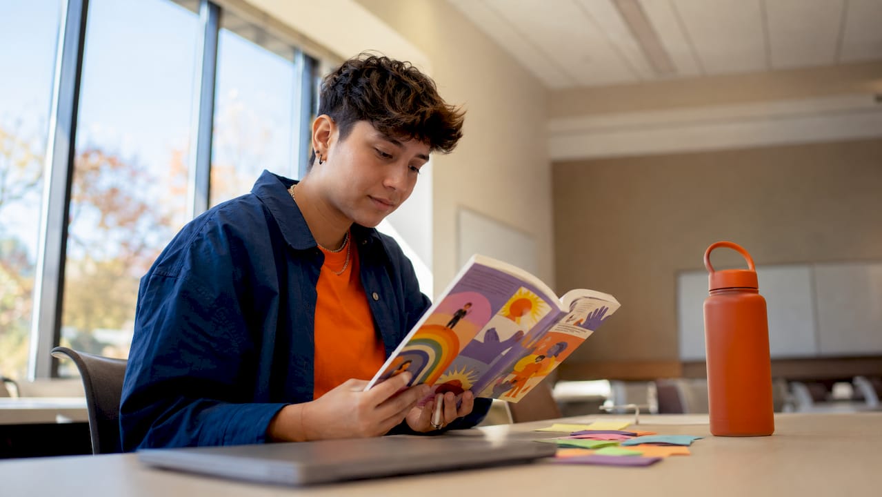 Nonbinary student reading LGBTQ+ career guidebook