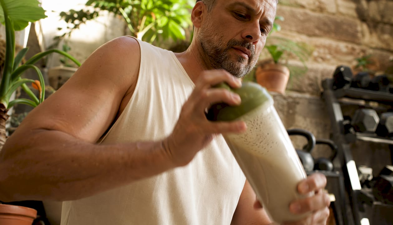 Man mixing plant-based protein shake in gym locker room