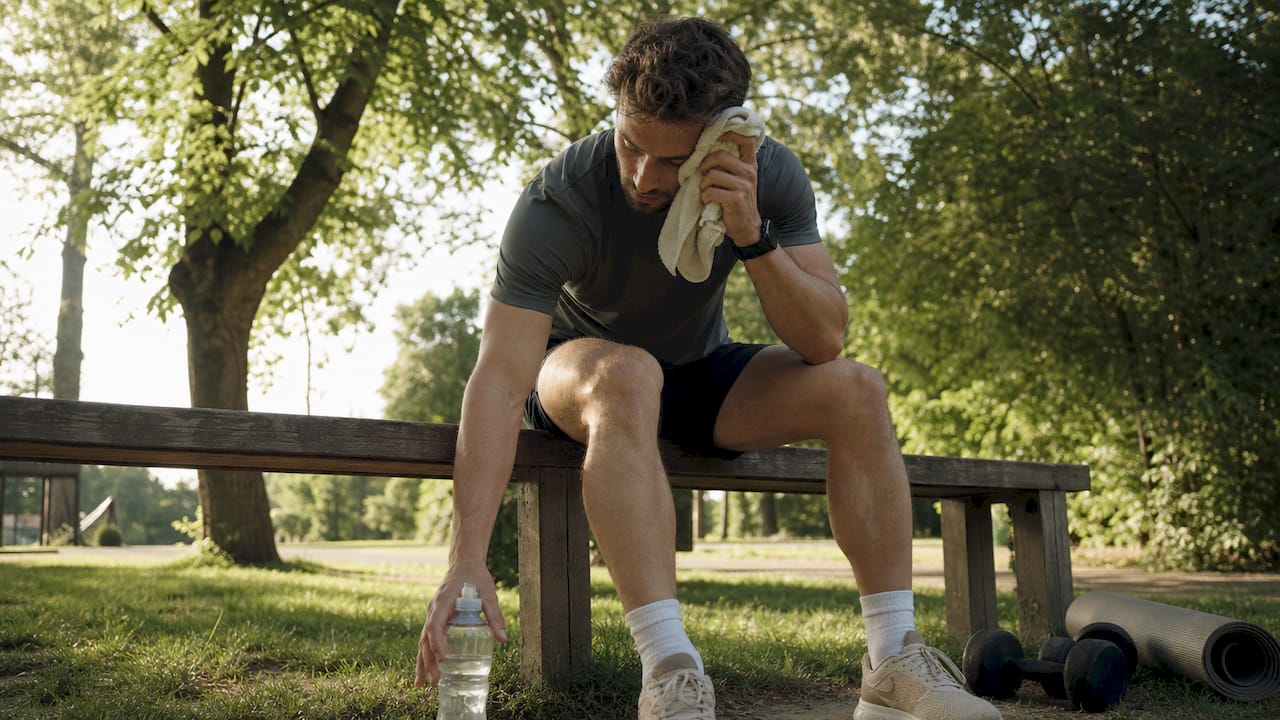 Man resting and drinking electrolyte drink in gym