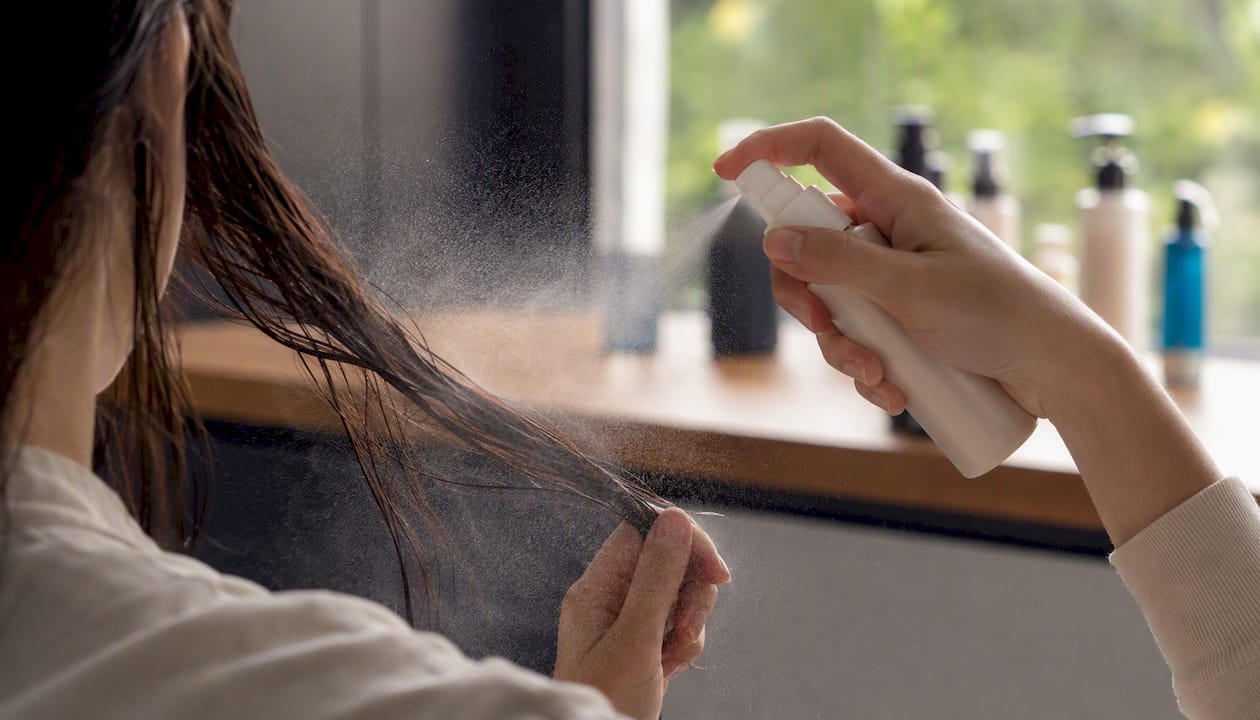 Hands spraying heat protectant on damp hair