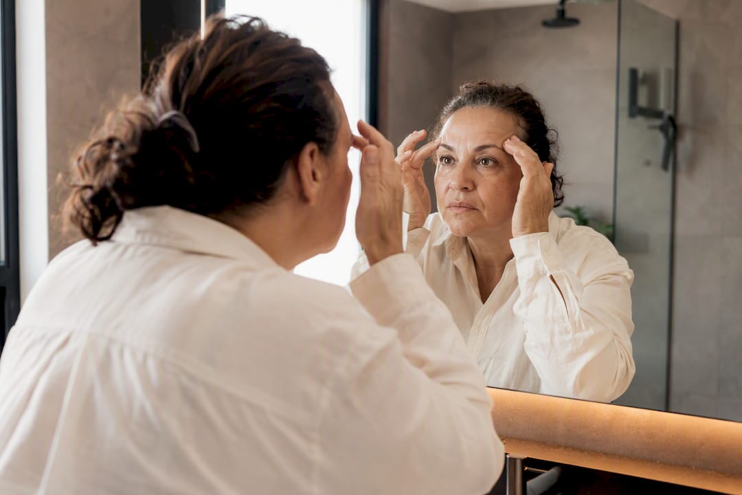 Persona que se mira al espejo revisando cómo le quedan las cejas y la línea del cabello.