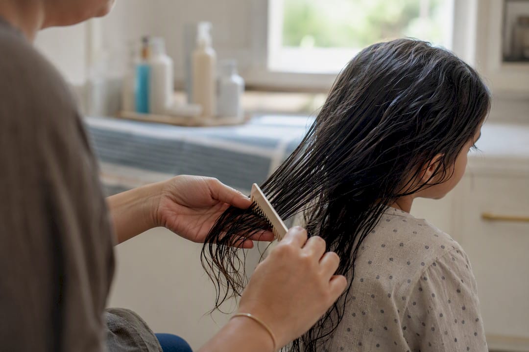 Hands detangling wet hair with wide-tooth comb