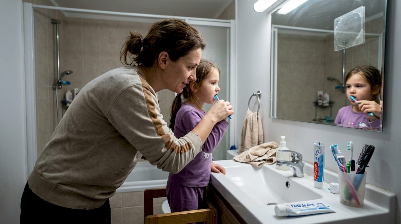 Un părinte care își ajută copilul să aibă grijă de dinți, arătându-i cum să se spele corect pe dinți și supraveghindu-l la fiecare pas, pentru ca micuțul să deprindă obiceiuri sănătoase încă de la început.