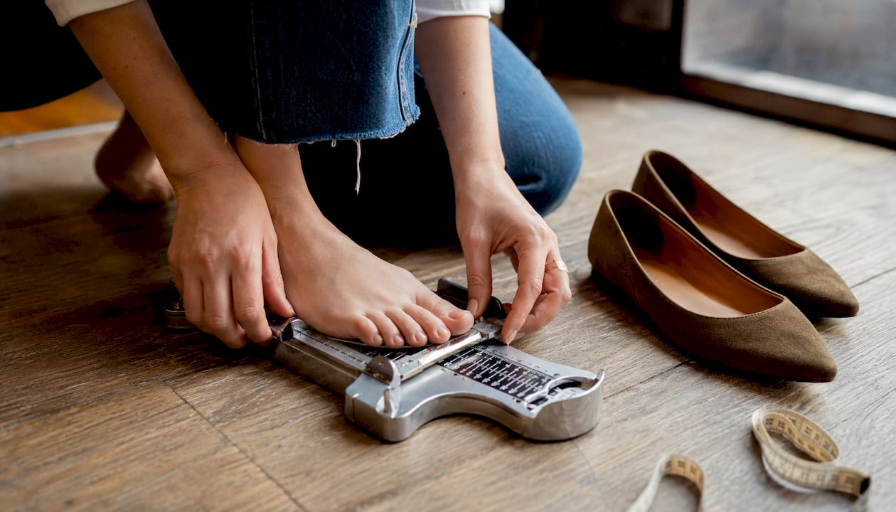 Hands measuring foot width with Brannock device