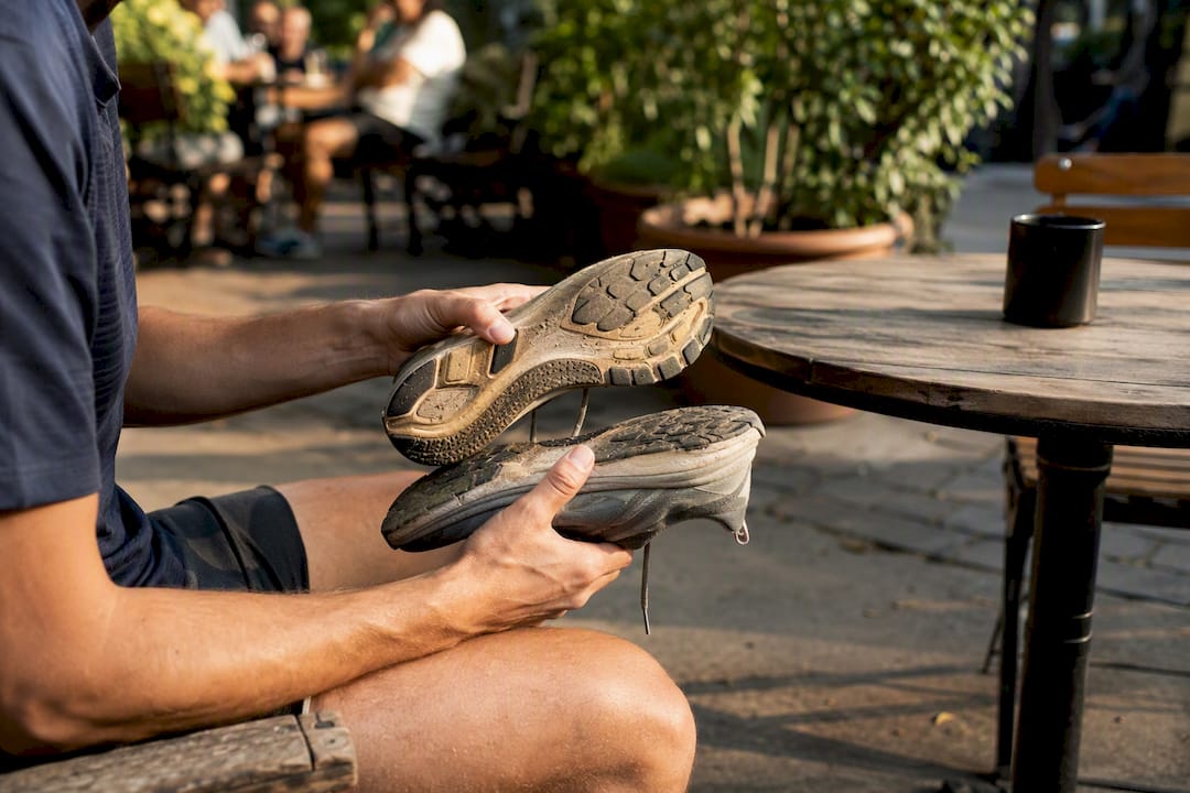 Hands inspecting worn running shoe outsole outdoors