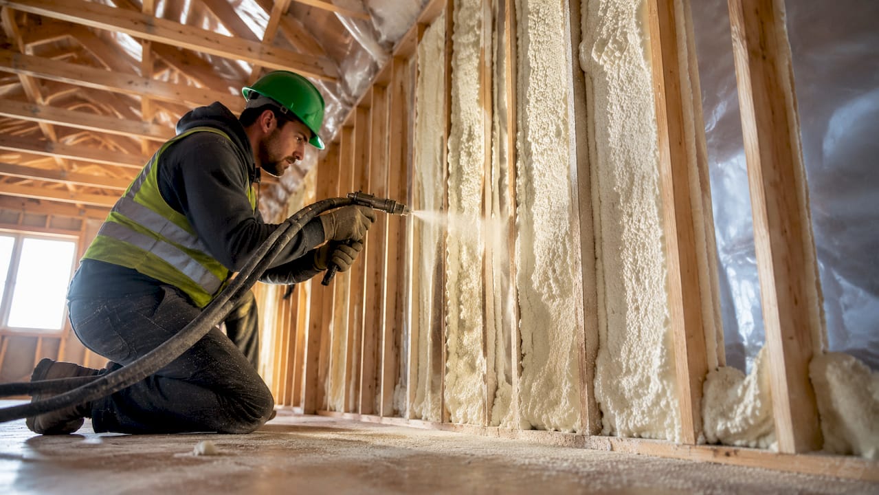 Worker spraying insulation in home wall cavity