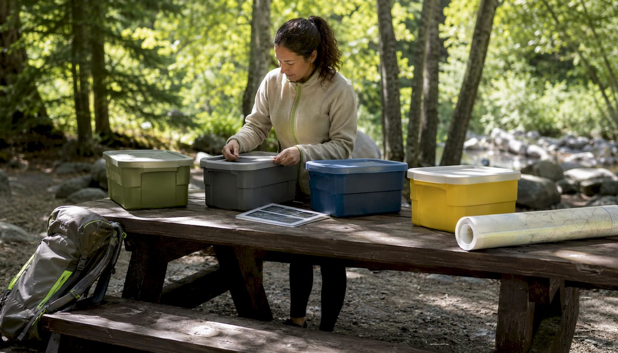 Hands organizing labeled camping gear bins indoors