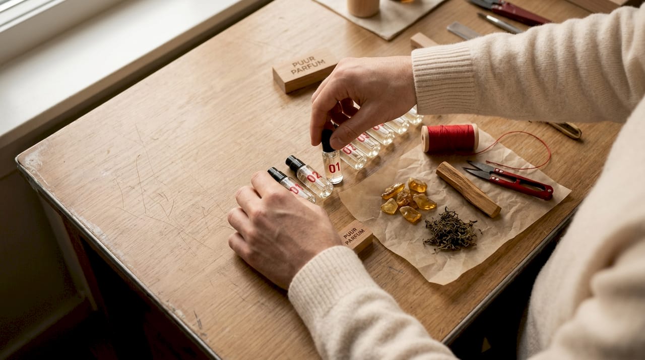 Handen die flesjes met amber, sandelhout en musk zorgvuldig ordenen.