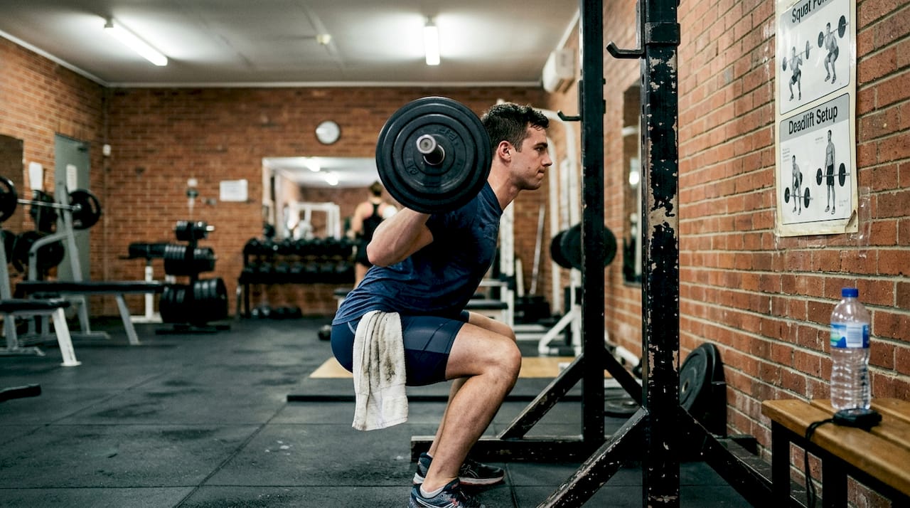 Male swimmer doing barbell squats in gym