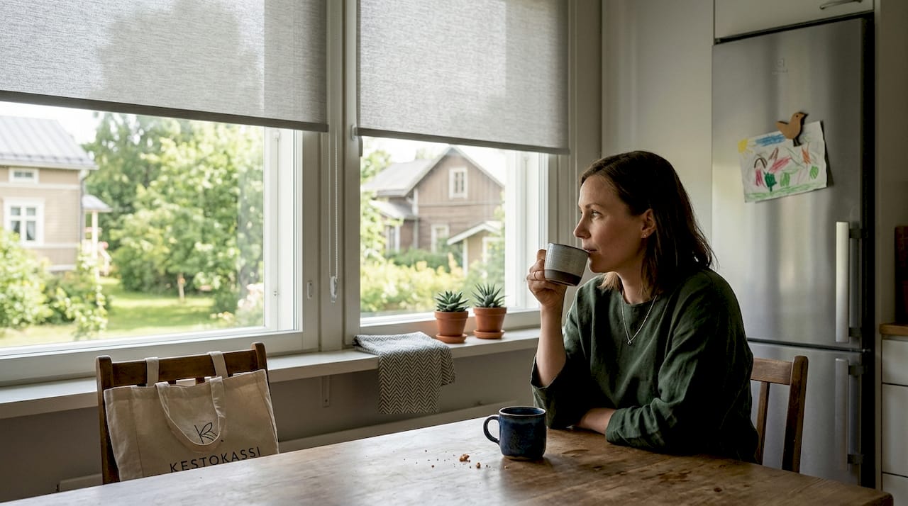 Nainen nauttii kahvihetkestä keittiössä, jossa on tyylikkäät sälekaihtimet.