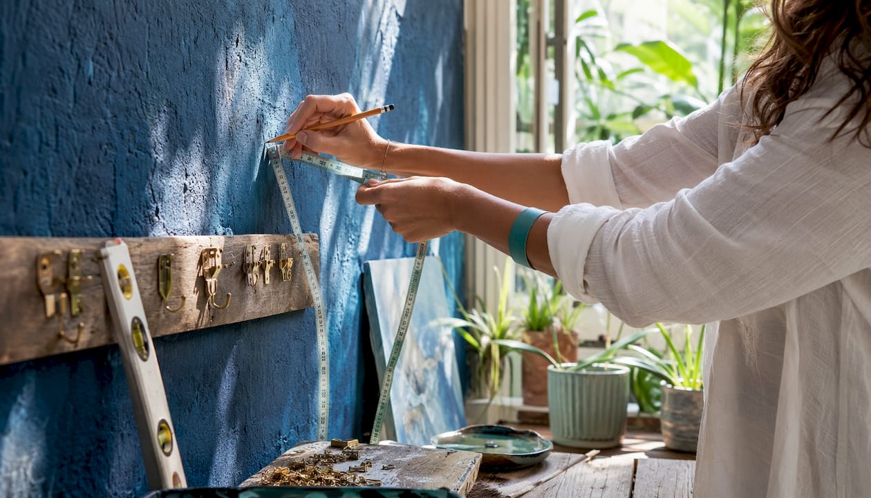Hands using stud finder and tools for hanging canvas