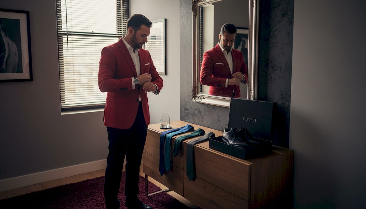 Een man past een opvallende blazer terwijl hij voor de spiegel staat.