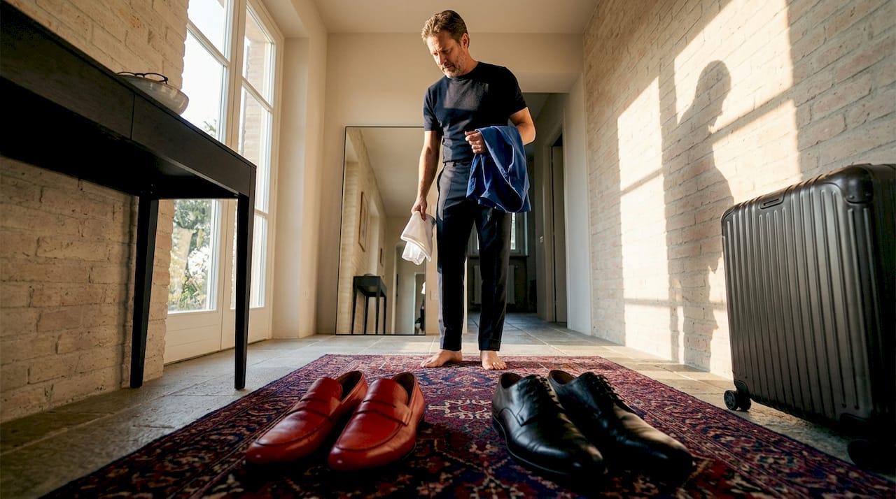 Un uomo si guarda allo specchio mentre cerca di scegliere le scarpe giuste da abbinare al suo outfit.