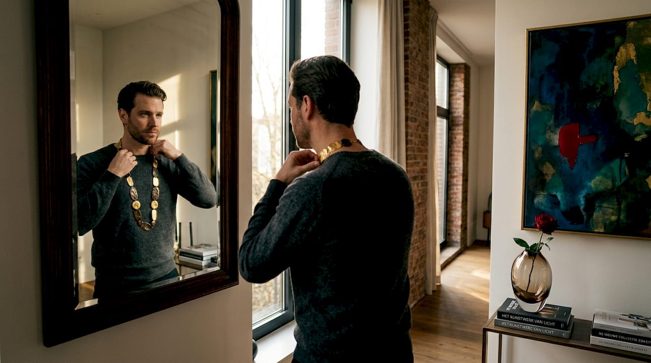 Een man staat bij de gangspiegel en brengt zijn opvallende ketting netjes in model.
