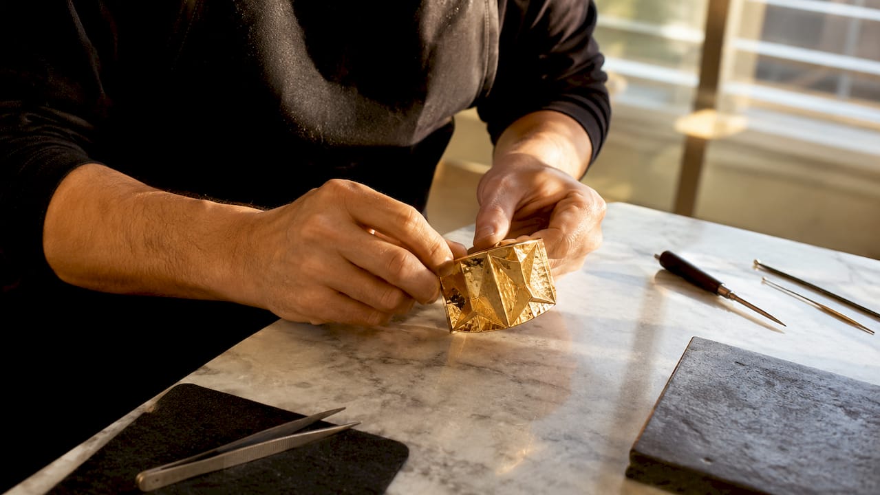 Des mains d’artisan façonnent avec précision un bracelet manchette en or, véritable œuvre d’art.