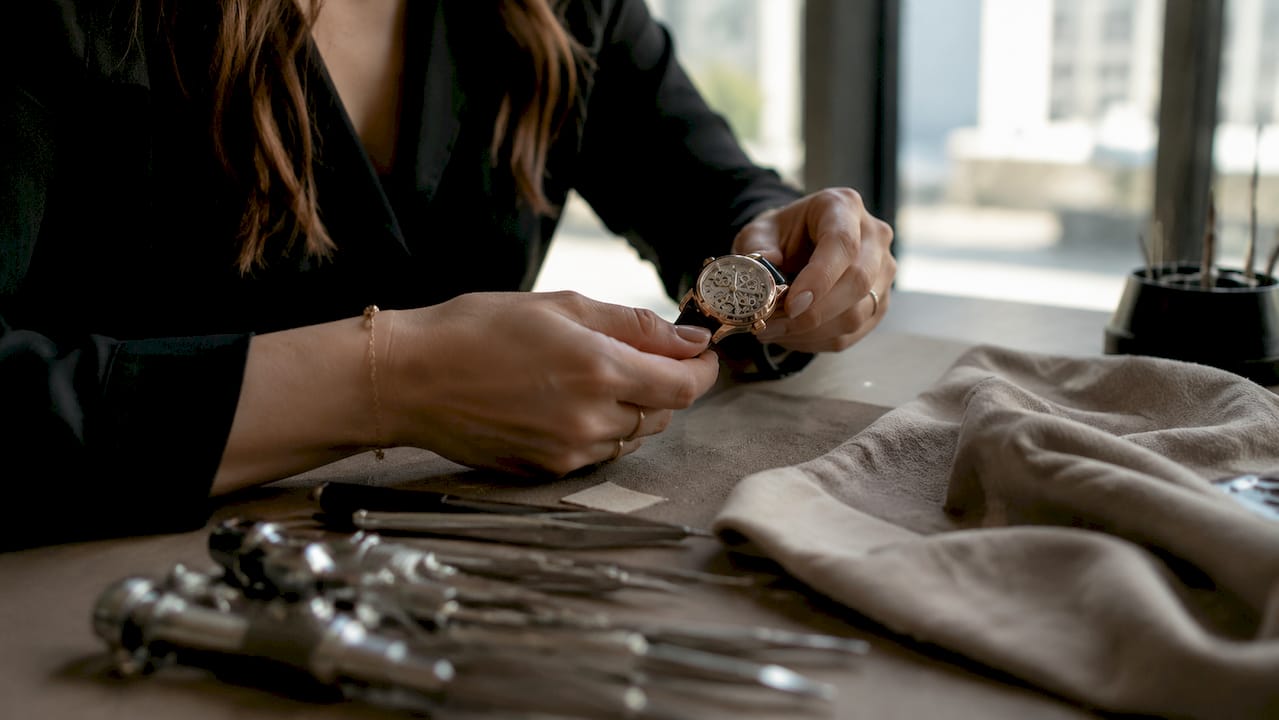 Un paio di mani attente osservano nei dettagli un orologio di alta orologeria, apprezzandone la raffinatezza artigianale.
