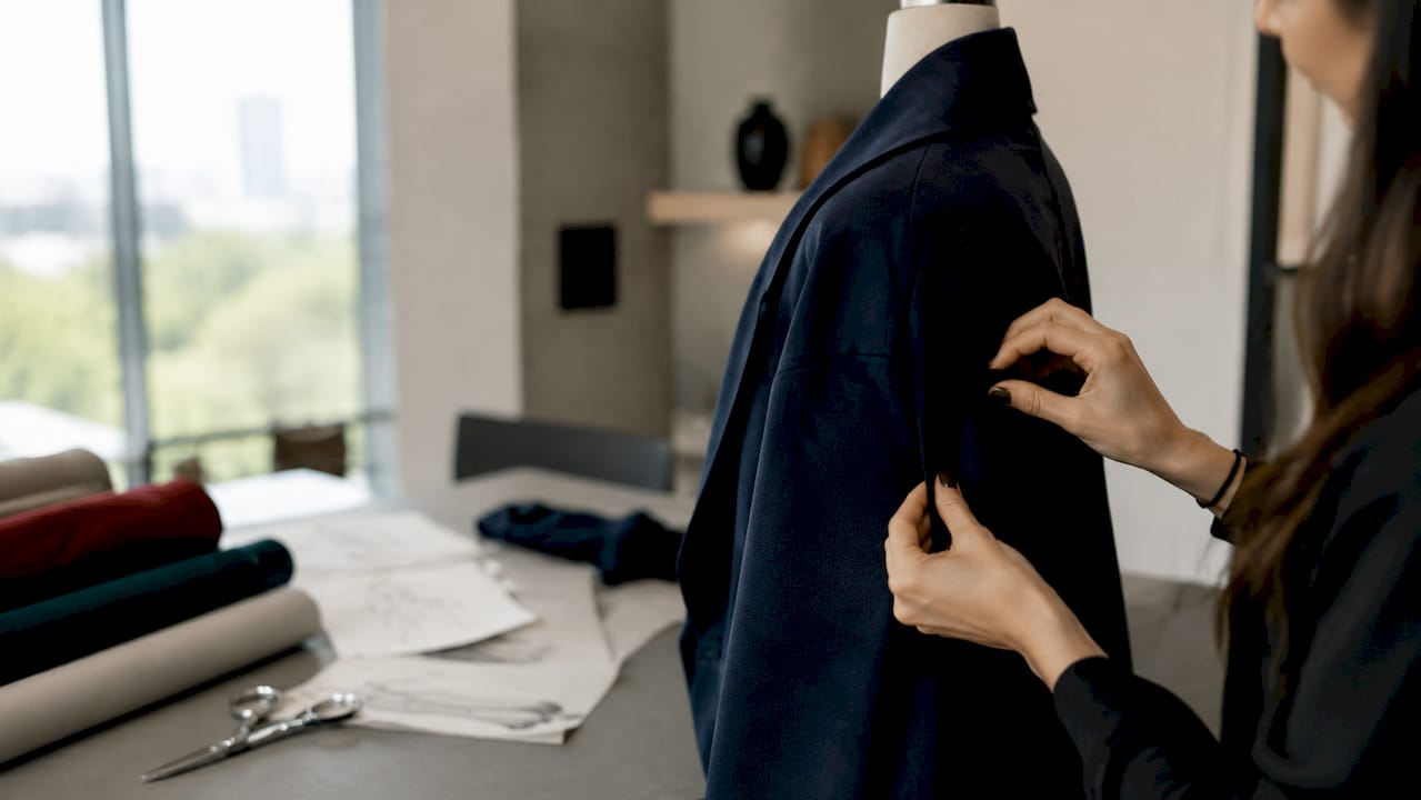 Unas manos trabajan con cuidado en el taller, dando forma a una chaqueta de corte amplio.