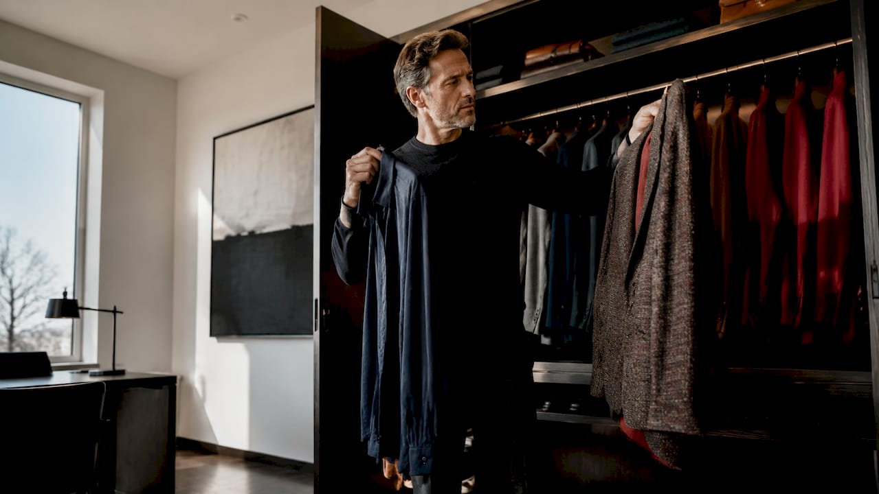 Un homme prend le temps de trier soigneusement ses vêtements dans son armoire, en les rangeant avec méthode.