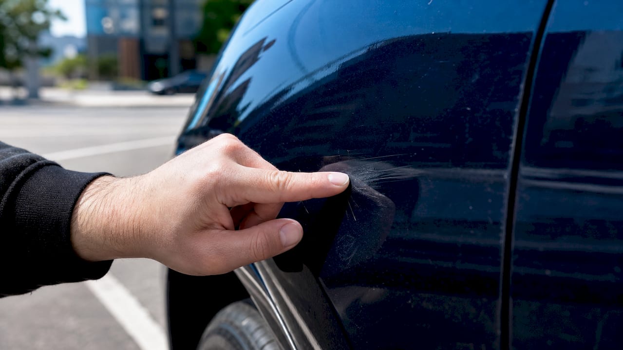 Close-up fingernail testing car scratch depth