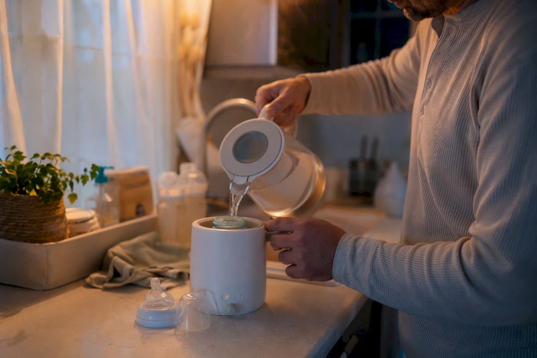 Partner's hands preparing baby bottle at kitchen counter