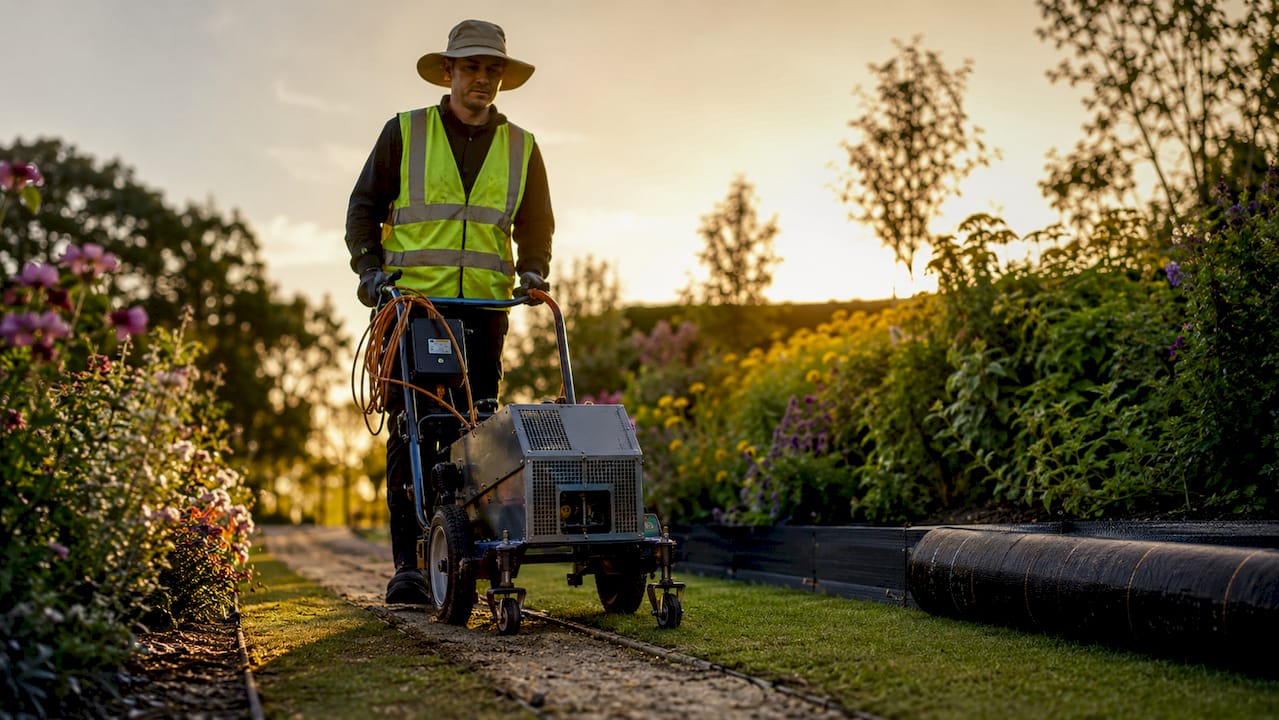 Technician operating electrical weed control machine in garden
