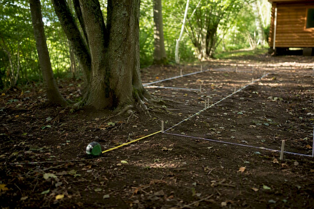 Measured log cabin outline near trees in a garden