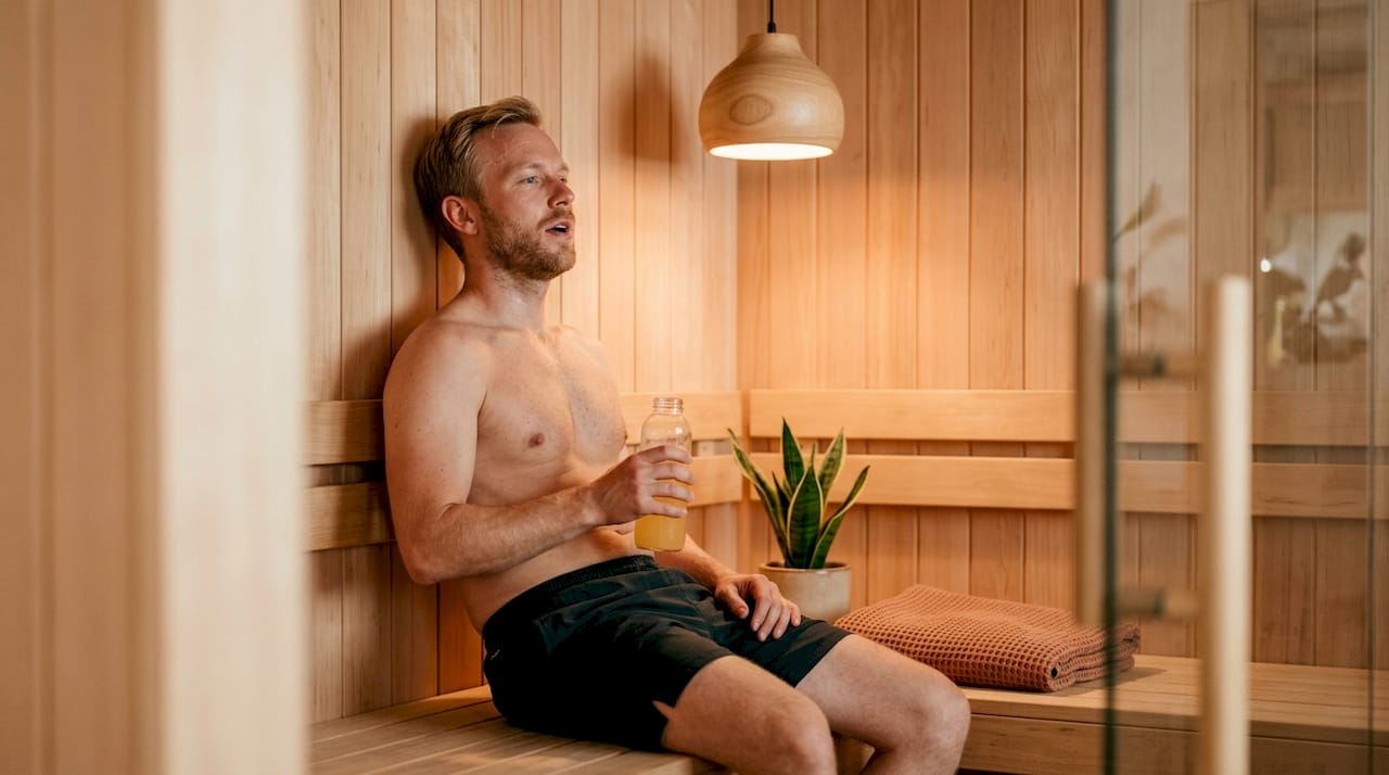 Et par hænder holder en flaske elektrolyt-vand tæt ved fjernbetjeningen til saunaen.