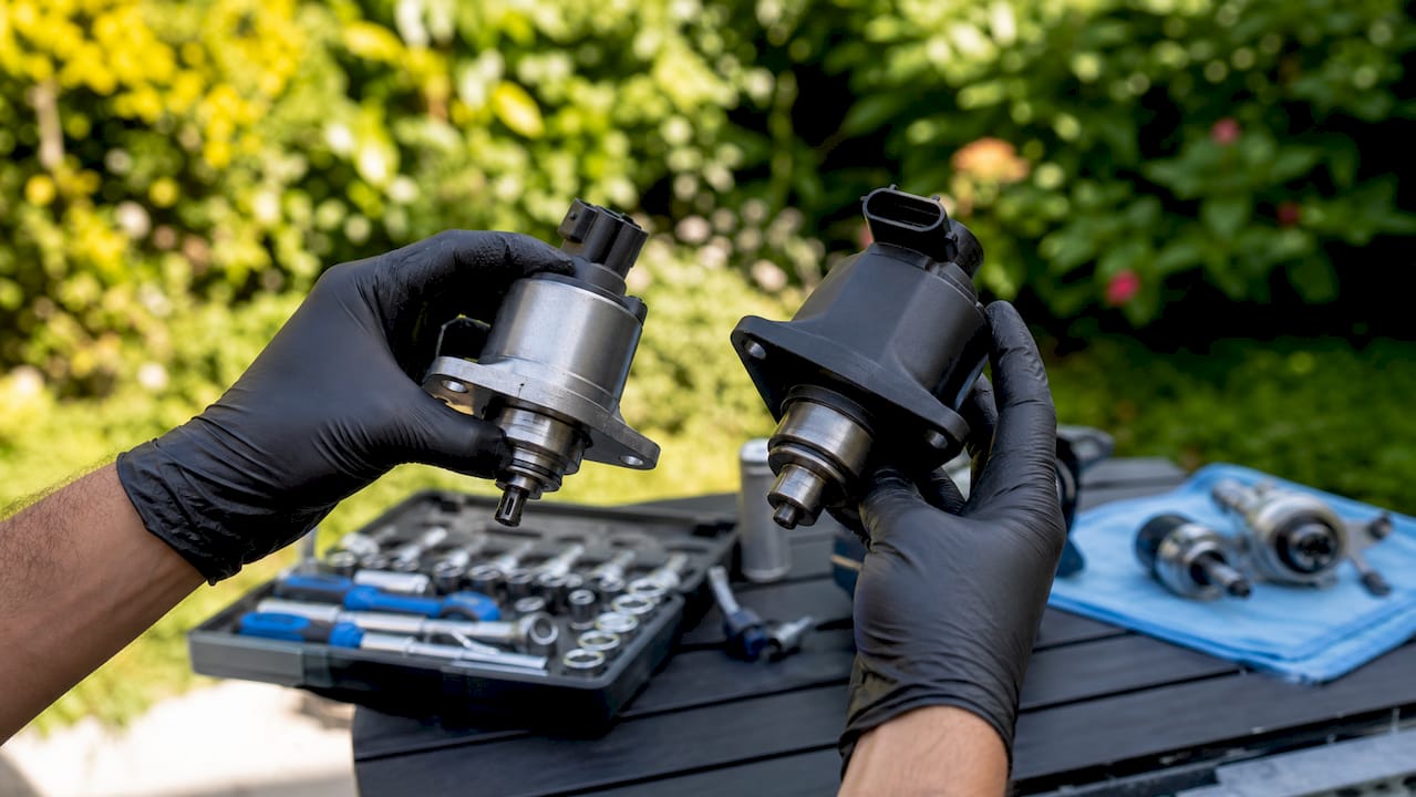 Hands comparing two vehicle parts in garage