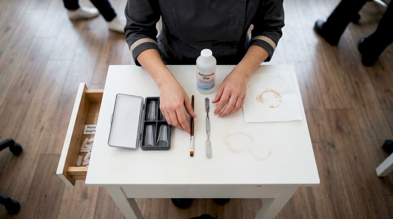 Una manicure prepara con cura gli strumenti per l’acrigel, sistemandoli ordinatamente sul tavolo prima di iniziare il trattamento.