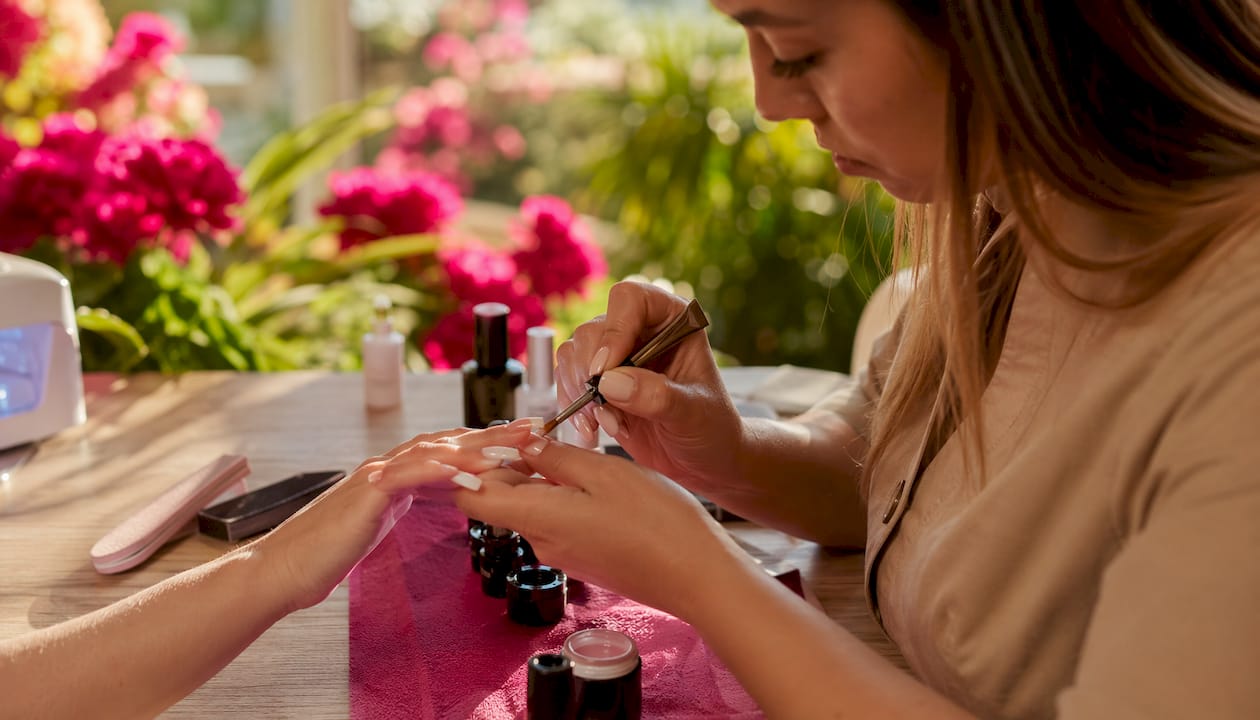 Dettaglio ravvicinato di mani mentre si stende il gel sulle unghie con l’aiuto degli strumenti professionali.