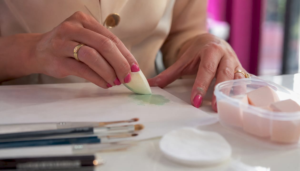 Mani che applicano il trucco con spugnette e pennelli