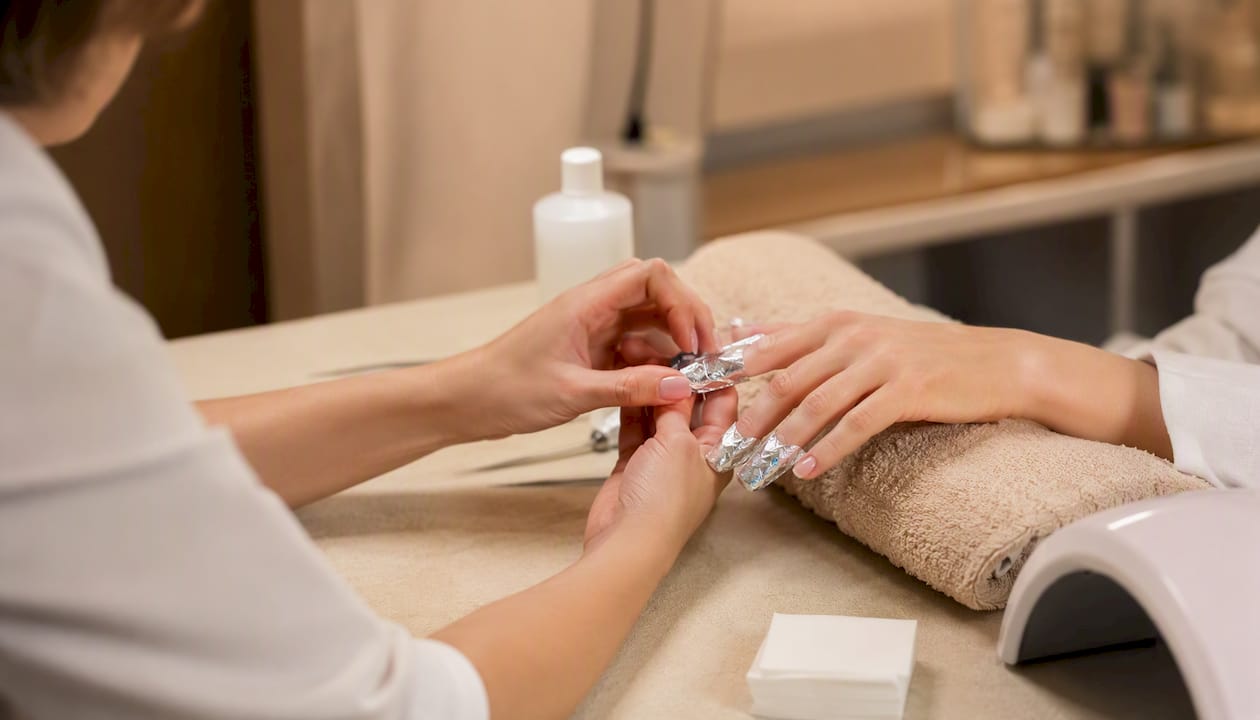 Le mani avvolte nella carta imbevuta di acetone per togliere il gel dalle unghie.