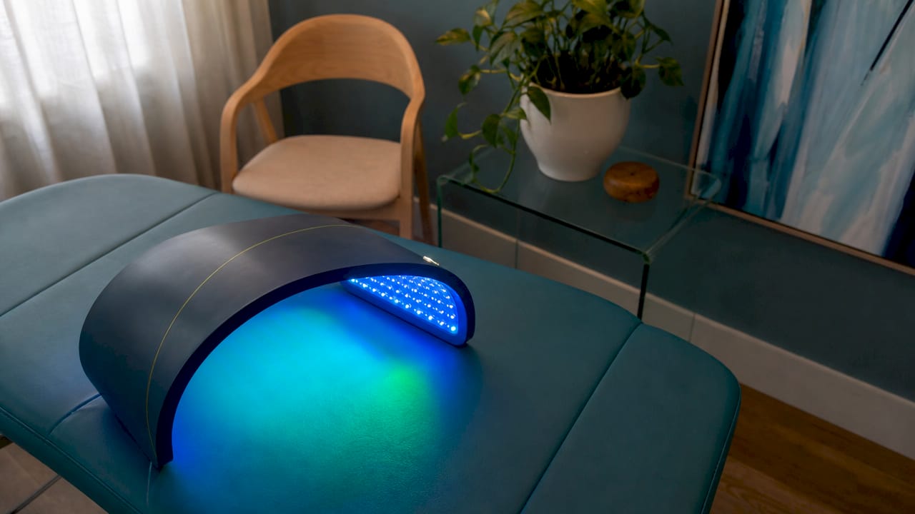 Sul divano, il dispositivo Celluma flessibile emette una luce blu e verde, creando un'atmosfera rilassante e tecnologica.